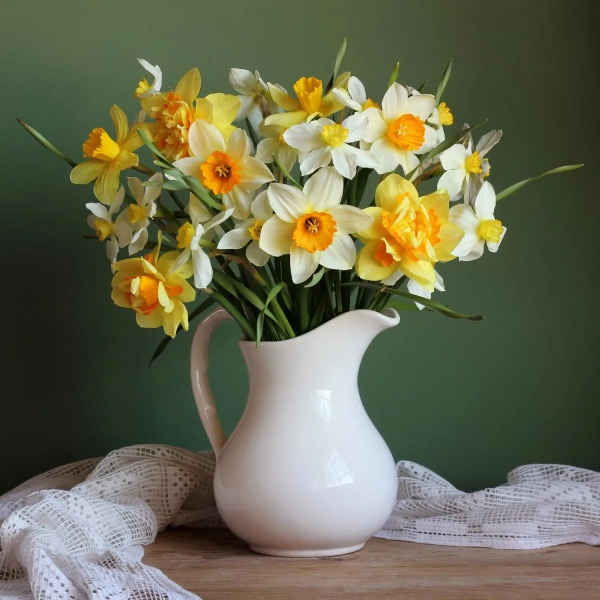 bouquet of daffodils in a white pitcher on a wooden table