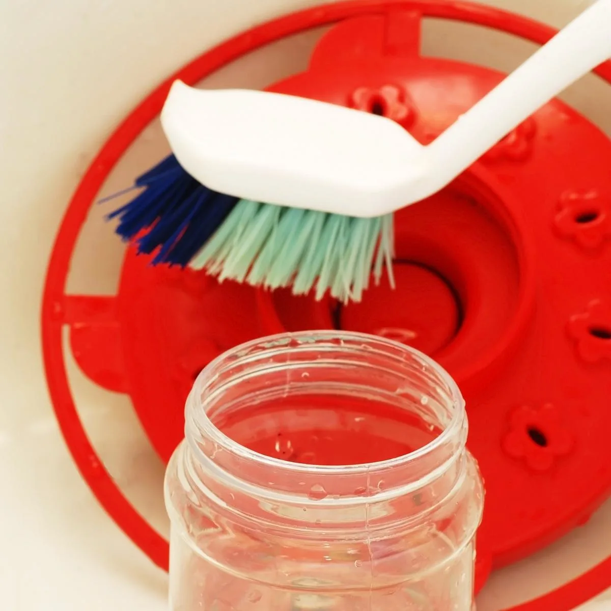 cleaning a hummingbird feeder with a brush and soapy water