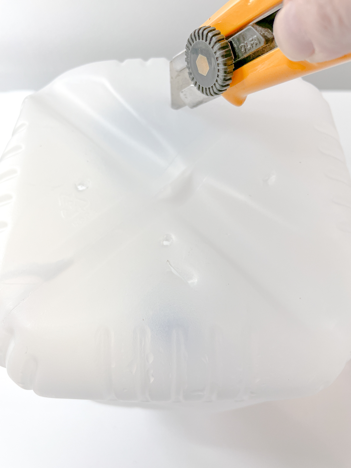 poking drainage holes in the bottom of a plastic milk jug with a box cutter